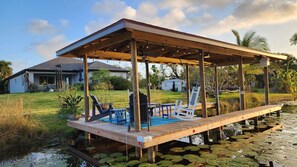 Une terrasse en bois, agrémentée de chaises et d’une table, entourée d’eau et de nénuphars.