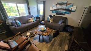 A cozy living room with two sofas, a coffee table, and a dog. -  Lakefront Retreat w/ Dock, Kayaks & Sunset Views – Peaceful Escape! (Lake Placid)