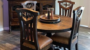 A dining area with a round wooden table, six chairs, a decorative mirror, and hanging pendant lights. -  Lakefront Retreat w/ Dock, Kayaks & Sunset Views – Peaceful Escape! (Lake Placid)