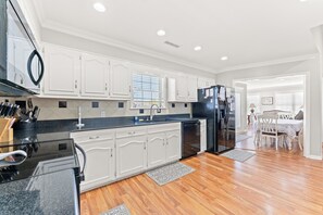 A modern kitchen with white cabinetry, a black refrigerator, and a dining area with a table and chairs.