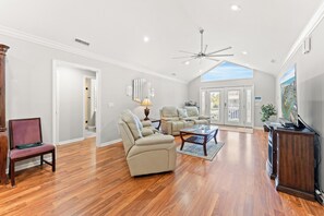 A spacious living room with a high ceiling, a ceiling fan, a large window, and a view of the outside. - Almost Retired - 3 Bed Cherry Grove Channel Home (North Myrtle Beach)