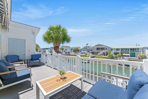 A deck with outdoor furniture, a palm tree, and a view of a marina with boats and buildings.