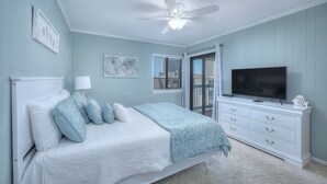 A bedroom with a bed, a dresser, a ceiling fan, and a TV.