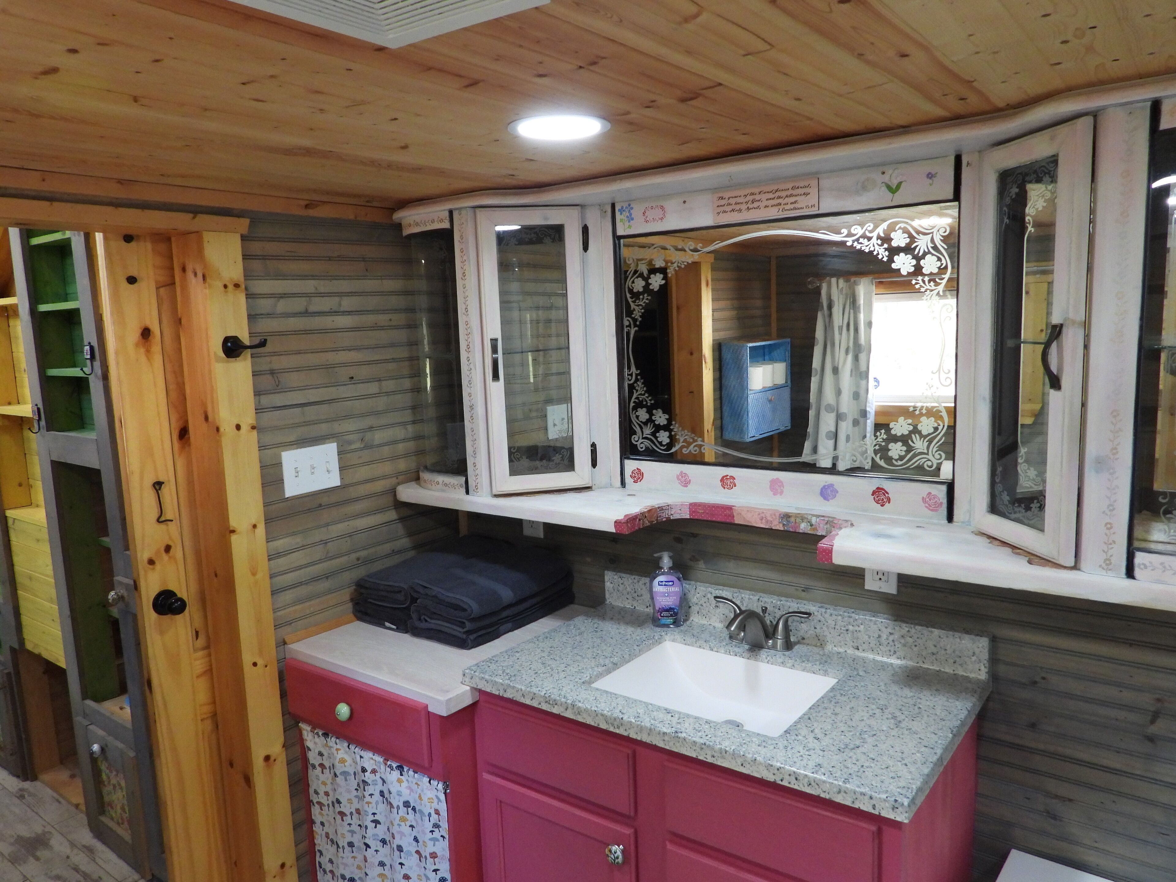 A bathroom with wooden ceiling, a sink with a mirror, and a towel rack.