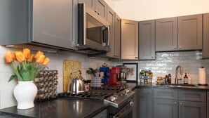 Een moderne keuken met grijze kastjes, een roestvrijstalen fornuis en een magnetron erboven. Op het aanrecht staat een vaas met tulpen, en er staan diverse keukenbenodigdheden en apparaten.