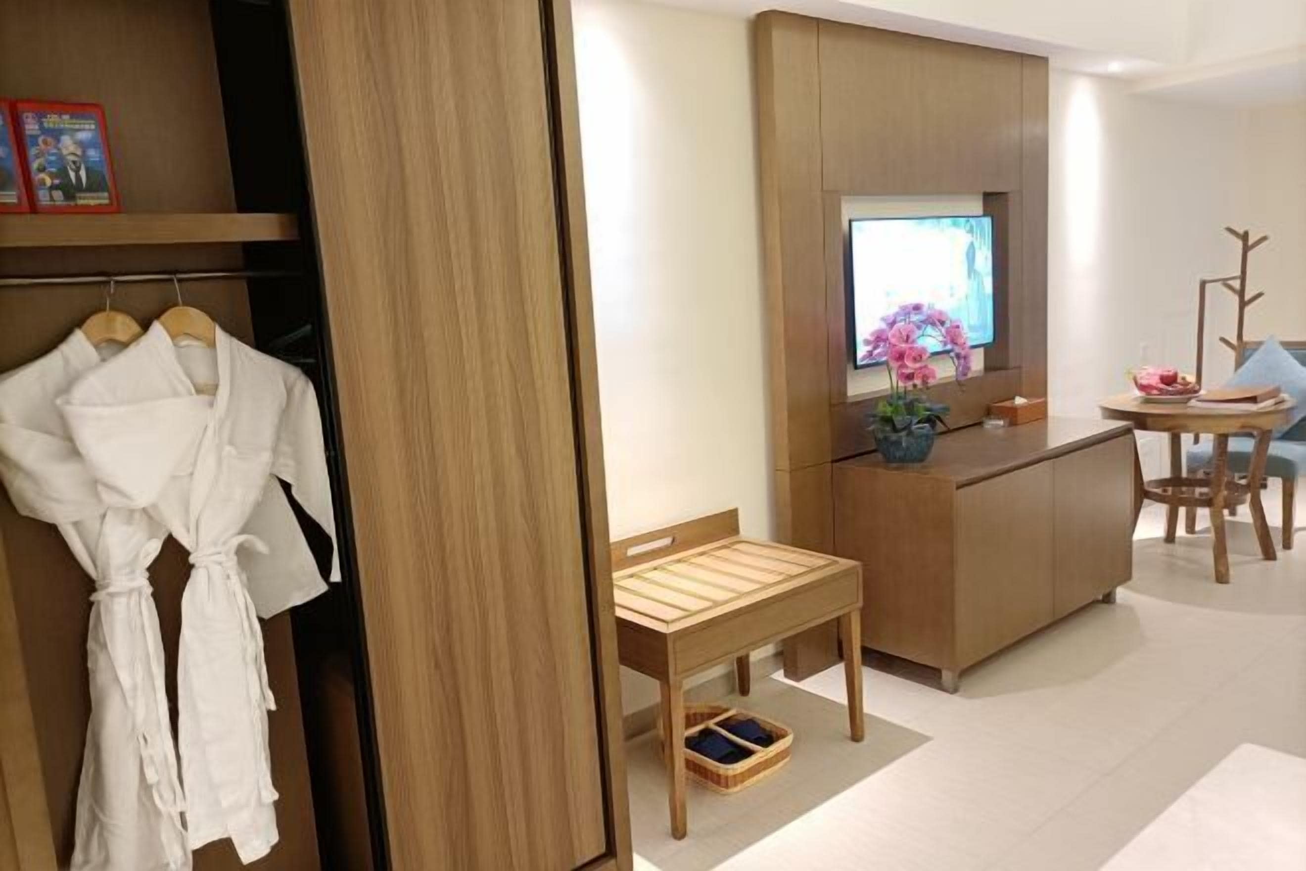 A modern hotel room with a wooden wardrobe, a small wooden table, a television, and a decorative plant.