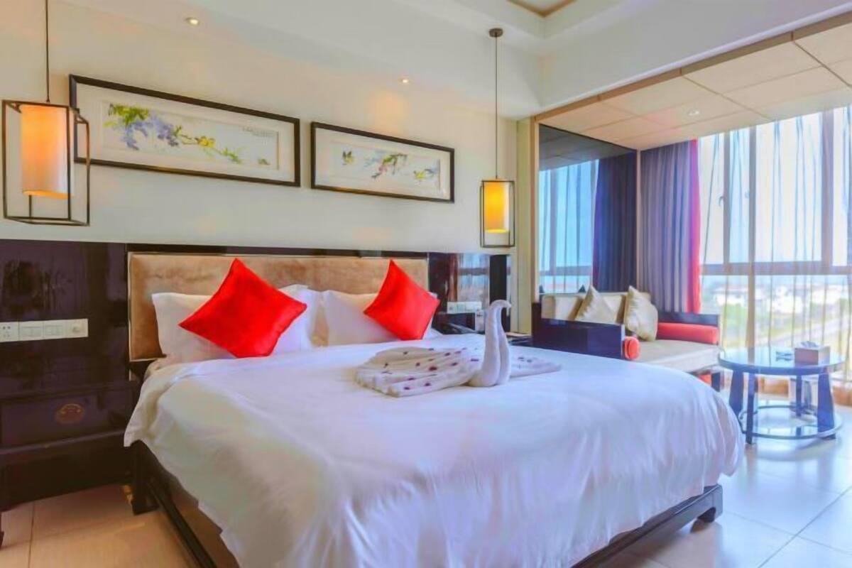 Een hotelkamer met een groot bed, rode kussens, een handdoek in de vorm van een zwaan en kunst aan de muur.