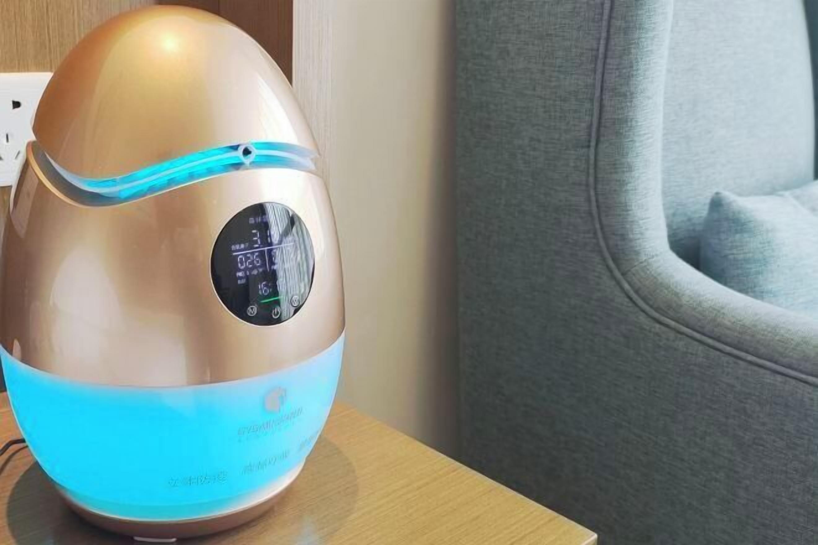 A modern, metallic air purifier with a digital display on a wooden surface.
