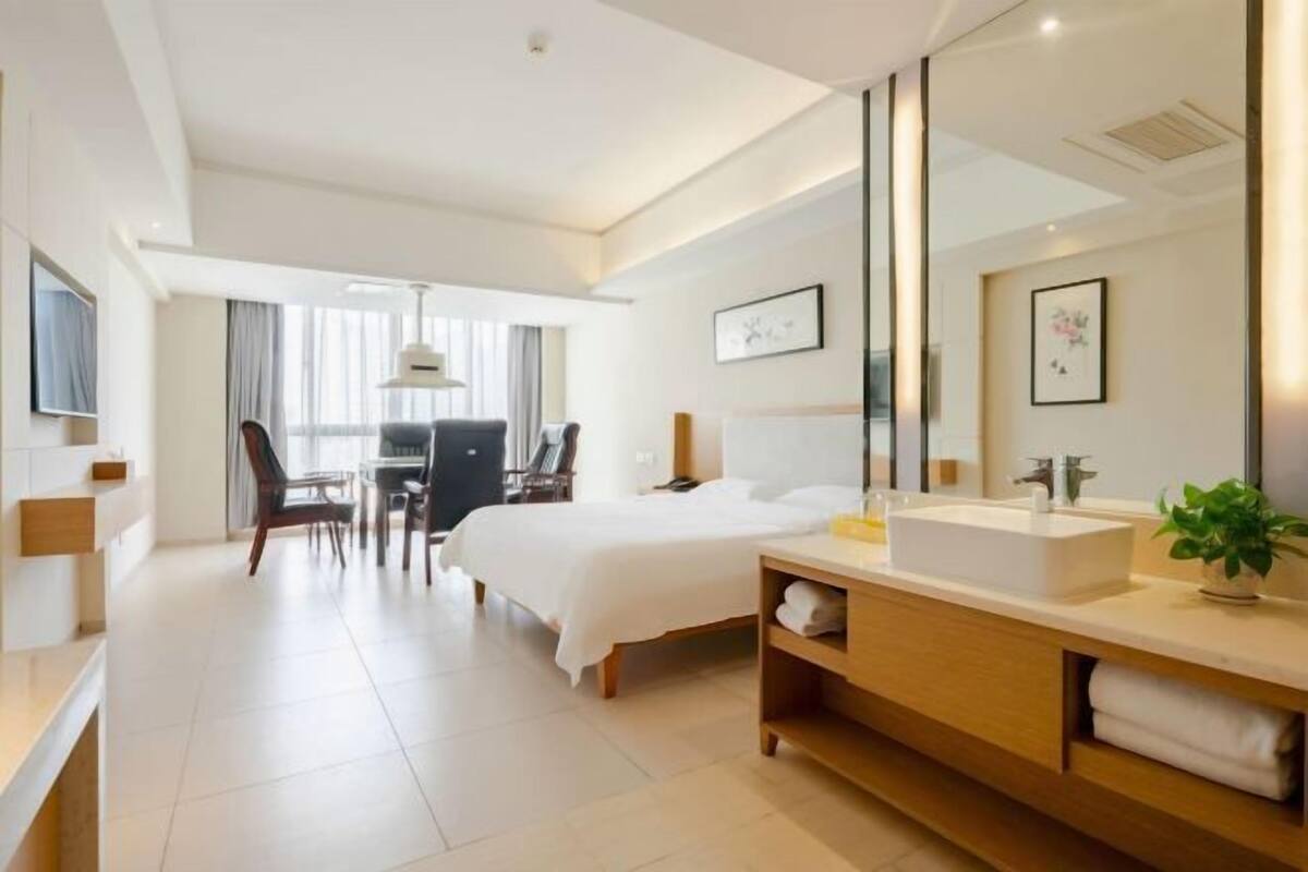 Een moderne hotelkamer met een groot bed, een nachtkastje met een wastafel, een stoel, een bureau en een grote spiegel.