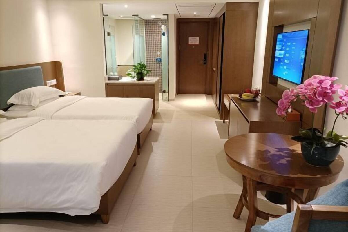 Een hotelkamer met twee bedden, een klein houten bureau, een televisie en een kamerplant.