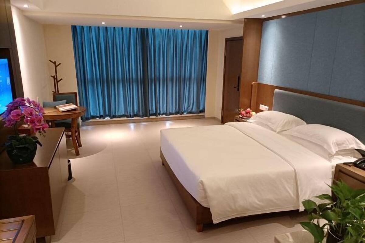 Een hotelkamer met een bed, een bureau, een stoel, een televisie en een groot raam met gordijnen.
