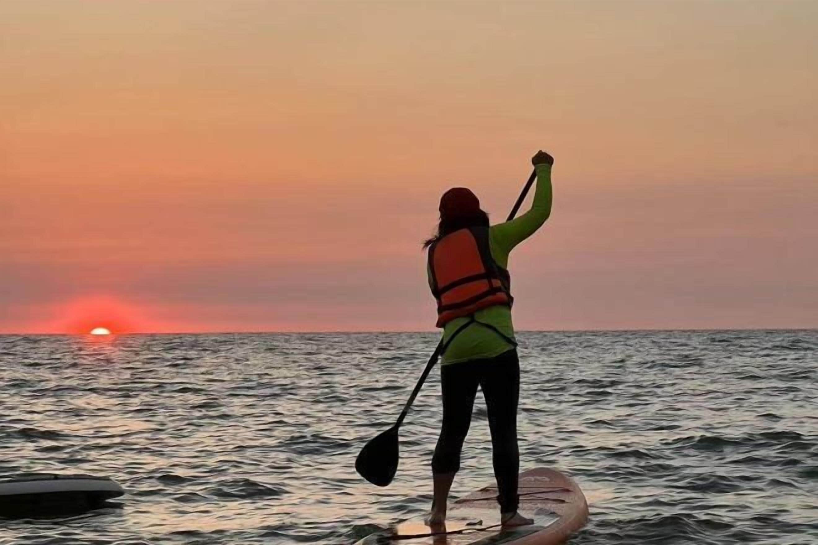 A person standing on a paddleboard in the water during sunset.