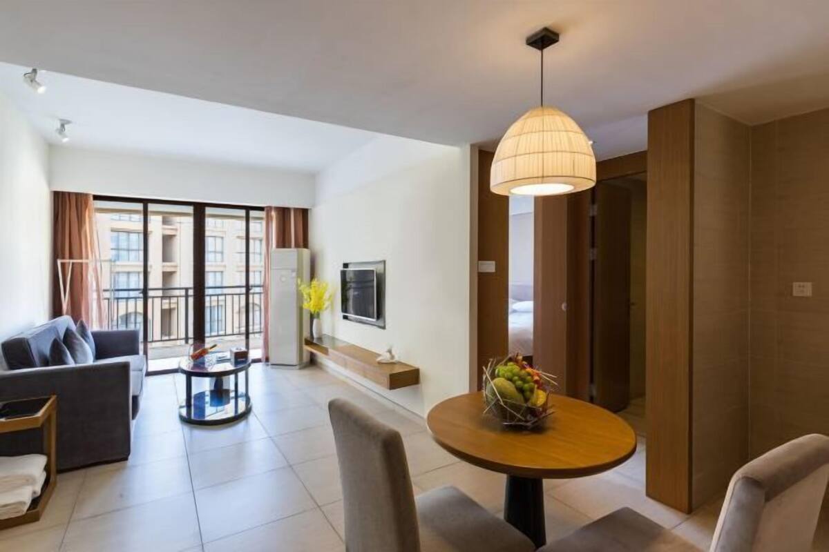 Een moderne woonkamer met een bank, een ronde tafel met fruit en een groot raam met gordijnen.