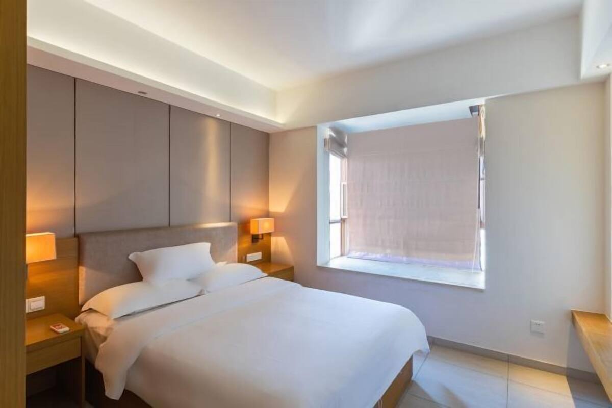 Hotelkamer met een bed, twee nachtkastjes met lampen, een raam met zonwering en een plafond met ingebouwde verlichting.