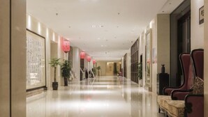 Un couloir d’hôtel avec un sol brillant, des chaises rouges et des plantes en pot.