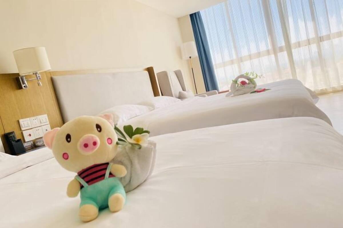 Een hotelkamer met twee bedden, een zacht varken op het bed en een vaas met bloemen.