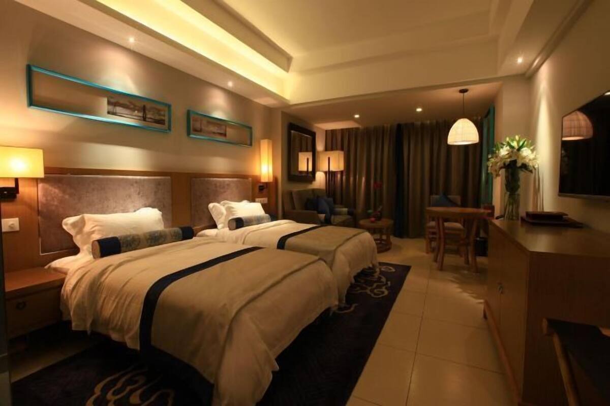 Een hotelkamer met twee bedden, een bureau, een stoel, een televisie en een kleine tafel met een bloevas.