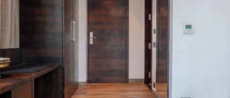 A hallway with a wooden floor, a dark wooden door, and a wall-mounted air vent.