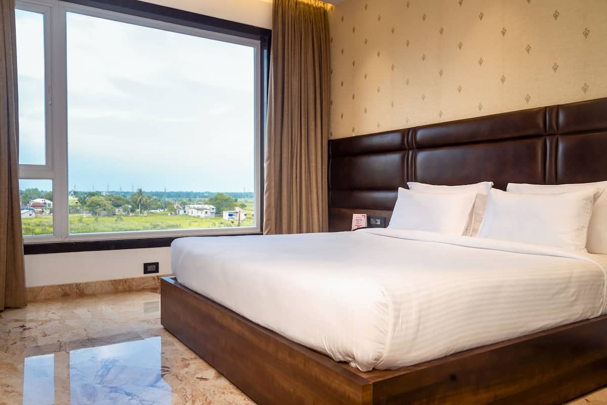 Una cama bien hecha con sábanas blancas en una habitación con un ventanal grande, pared con estampado y cabecera marrón.