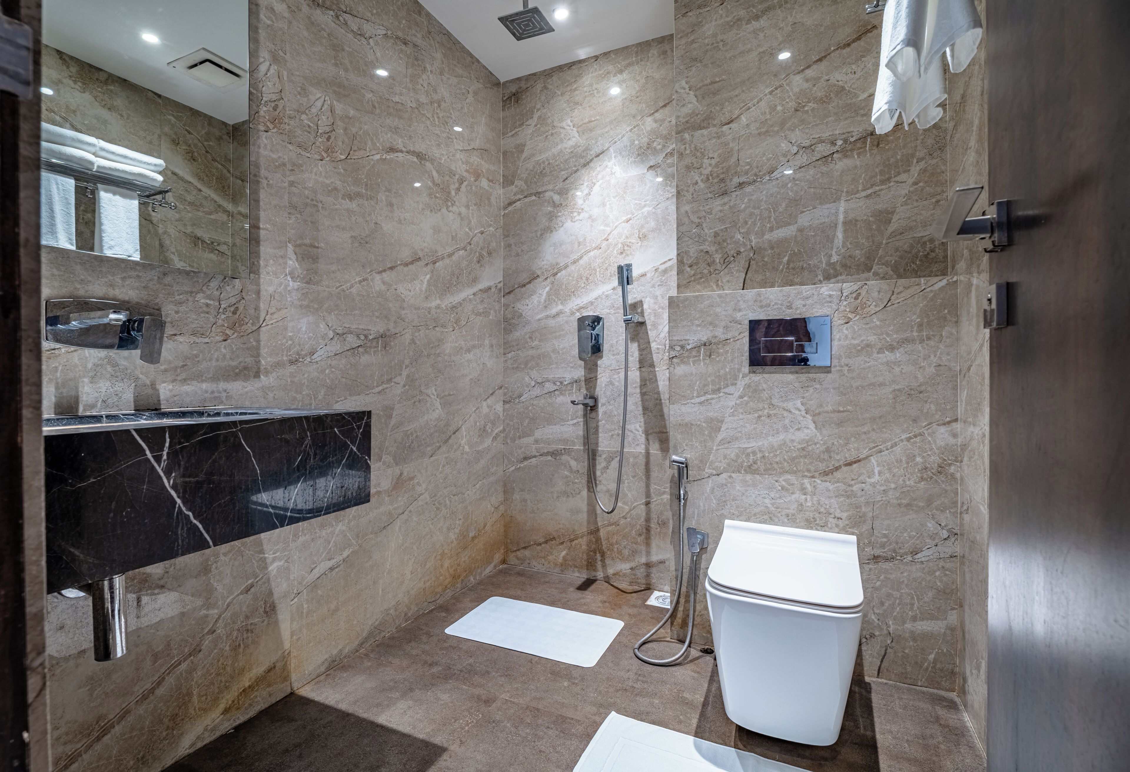 Et moderne badeværelse med marmorvægge, en sort vask, en bruseniche og et toilet.