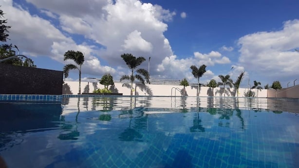 A swimming pool with clear blue water, surrounded by palm trees and a clear sky. - Econest Hotel (Rampurhat)