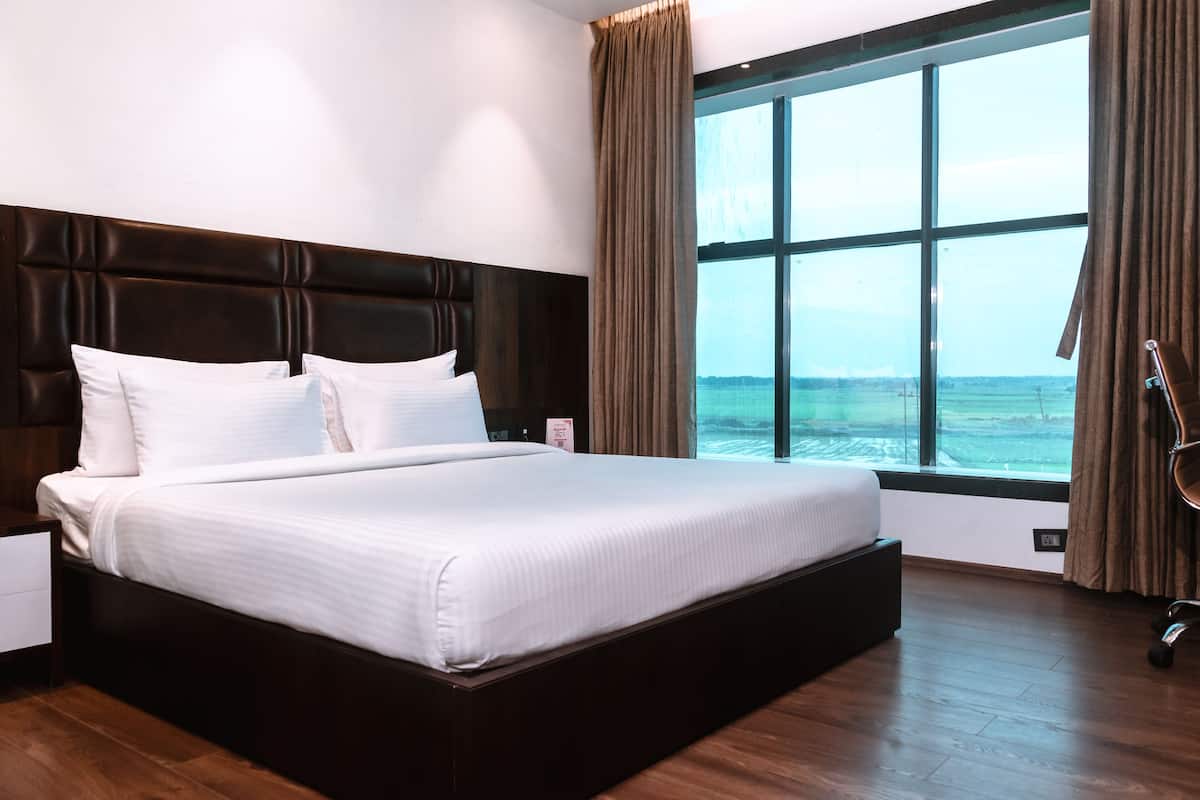 Una cama grande con cabecera oscura, ropa de cama blanca y vista al mar a través de un amplio ventanal con cortinas.