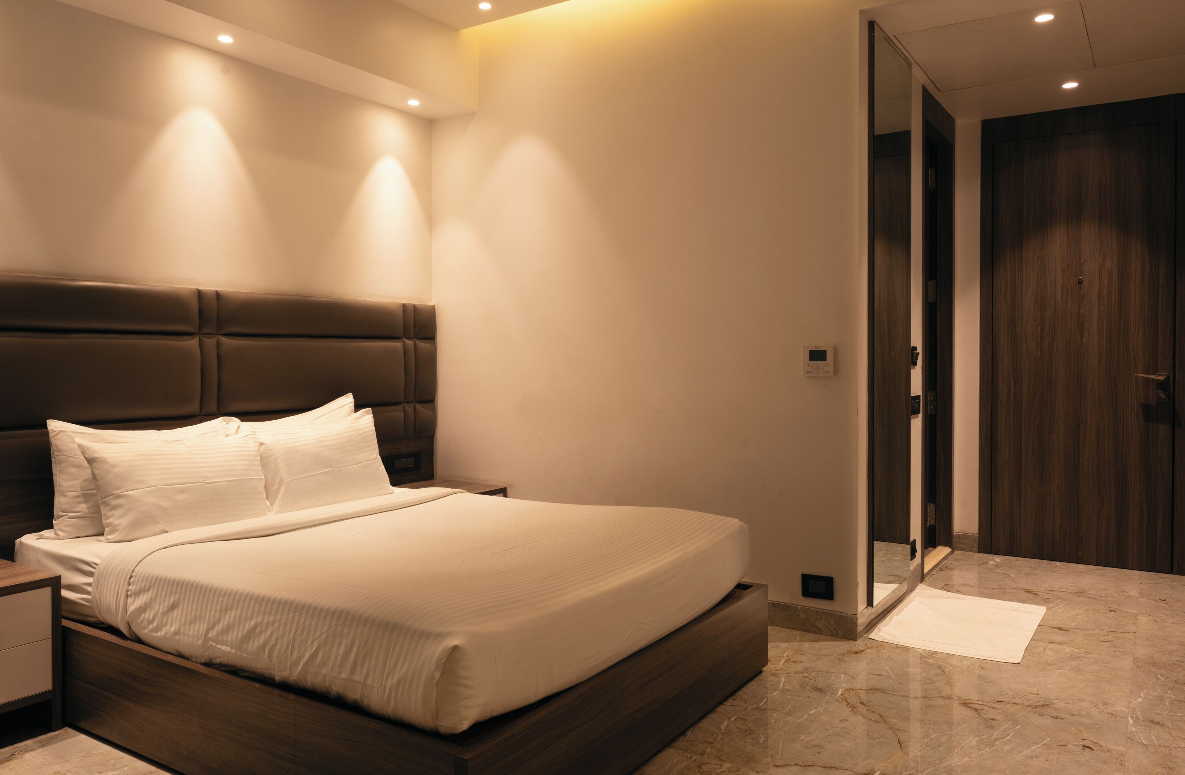 Une chambre à coucher moderne avec un grand lit, des tables de chevet, une tête de lit en bois et une porte.
