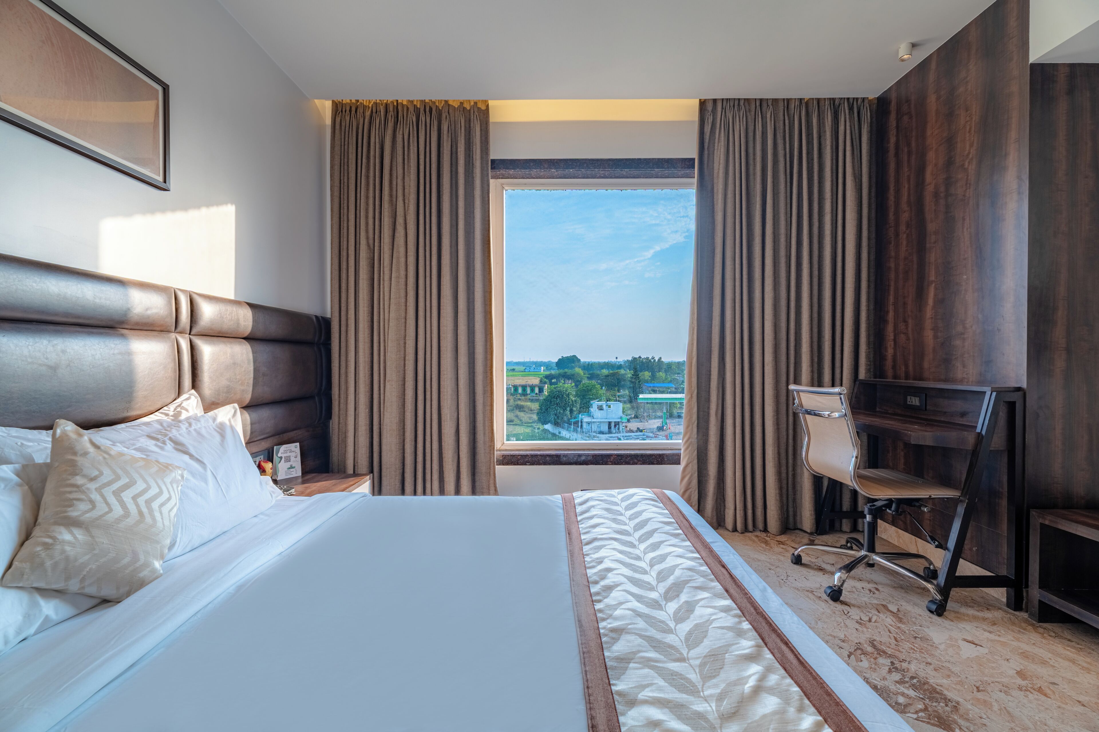 A hotel room with a large bed, a desk, and a view of the cityscape.