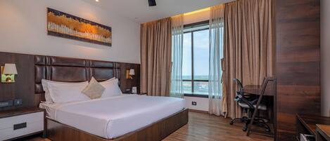 A hotel room with a large bed, a ceiling fan, a nightstand, a desk, a chair, and a window with curtains.