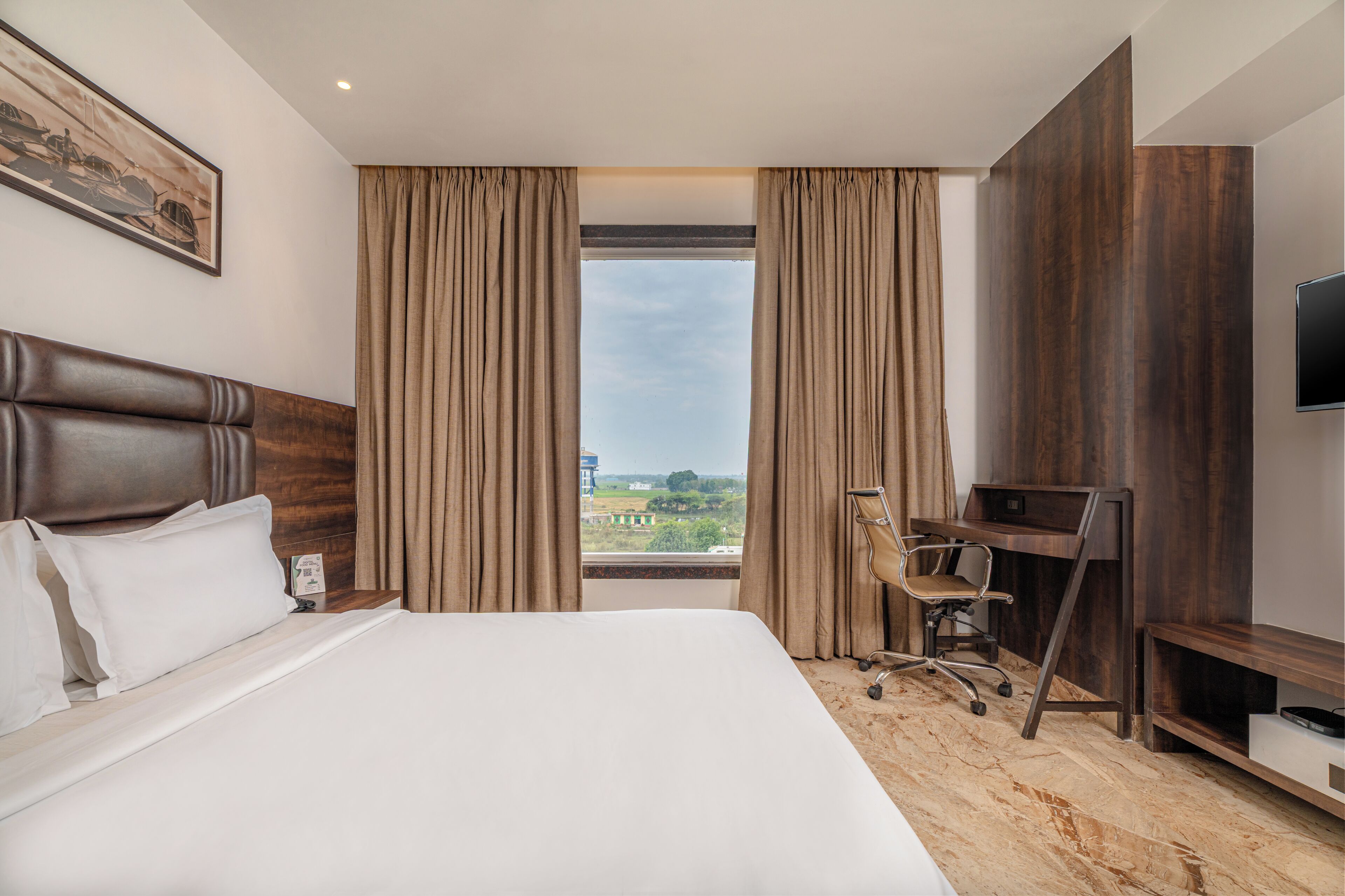 A hotel room with a large bed, a desk, a chair, a TV, and a window with curtains.