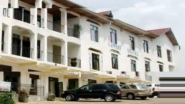 Un hotel de varios pisos con fachada blanca, balcones y un estacionamiento con varios automóviles.