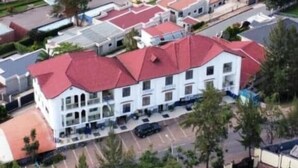 A large building with multiple red-roofed sections, surrounded by green fields and sparse trees. - DV Appart Hotel (Kigali)
