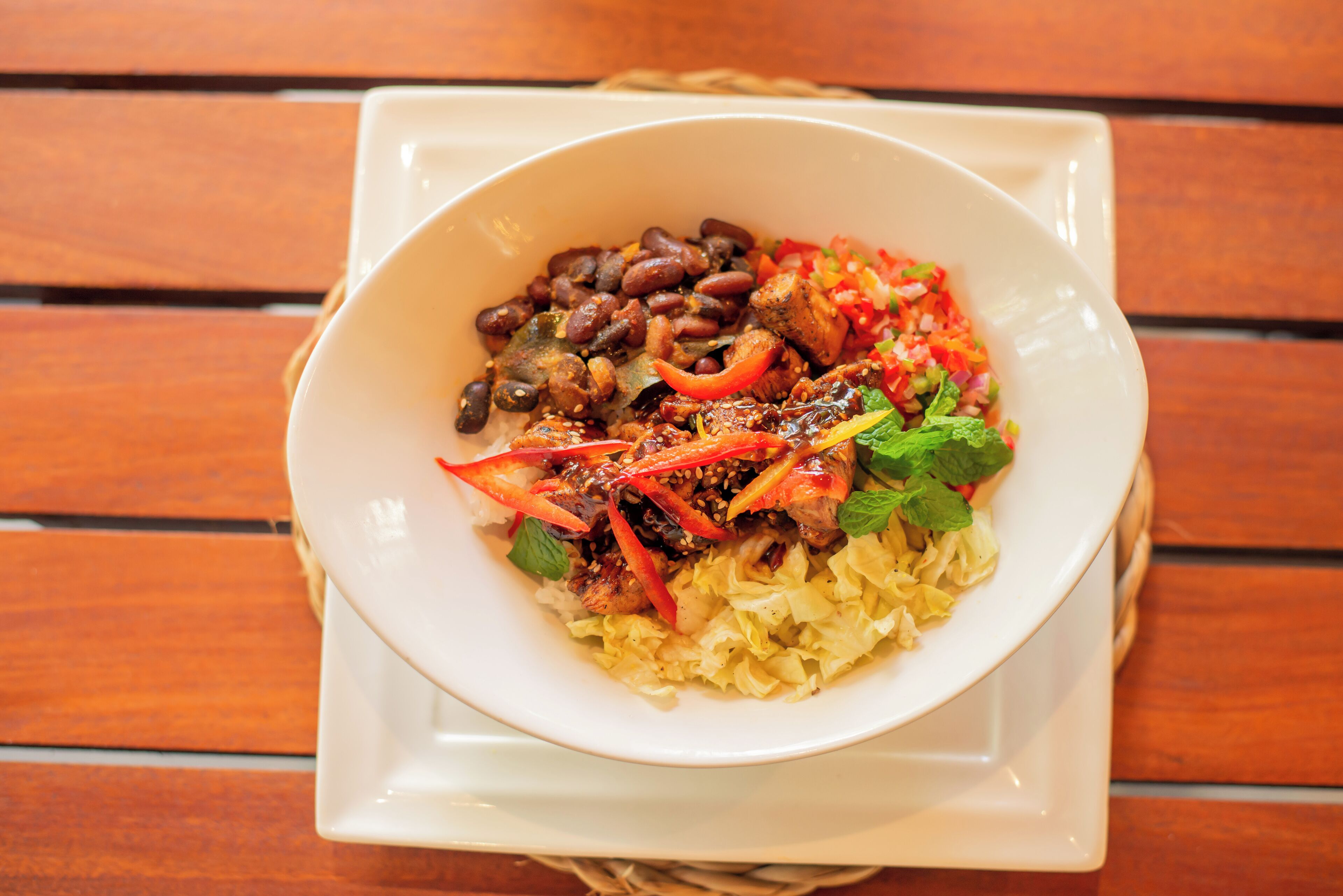 A bowl of food with beans, meat, and vegetables on a wooden table.