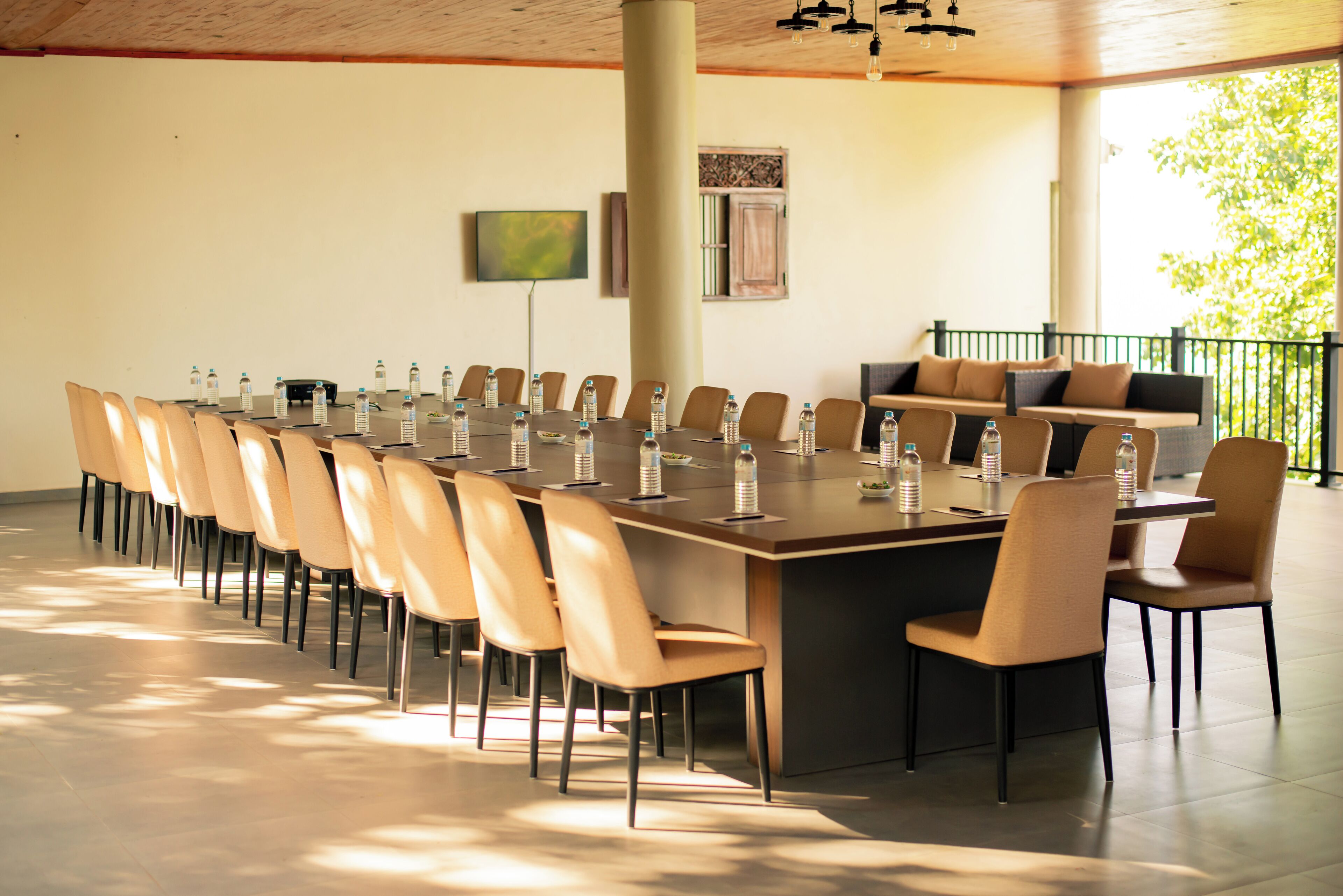 A conference room with a long table, chairs, water bottles, a sofa, and a TV on the wall.