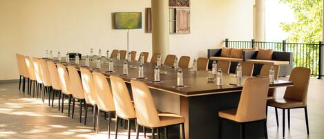 A conference room with a long table, chairs, water bottles, a sofa, and a TV on the wall.