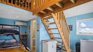 Una habitación con literas, escalera de madera, kitchenette y ventana con vistas.