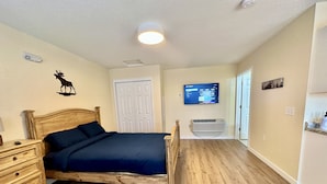 A bedroom with a wooden bed, a nightstand, a wall-mounted TV, and a white door. - Hot Tub Cozy Cottage in Colorado Springs (Colorado Springs)