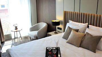 A neatly made bed with a tray of glasses and a feather quill, a bedside lamp, and a chair in a hotel room.