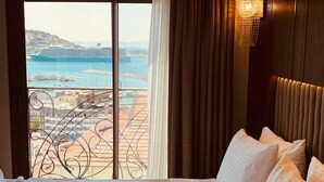 A hotel room with a large window offering a view of a cruise ship and a marina. - Monalisa (Kusadasi)