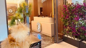 A hotel reception area with a modern design, including a reception desk, a large mirror, and a decorative wall with a circular emblem. - Monalisa (Kusadasi)