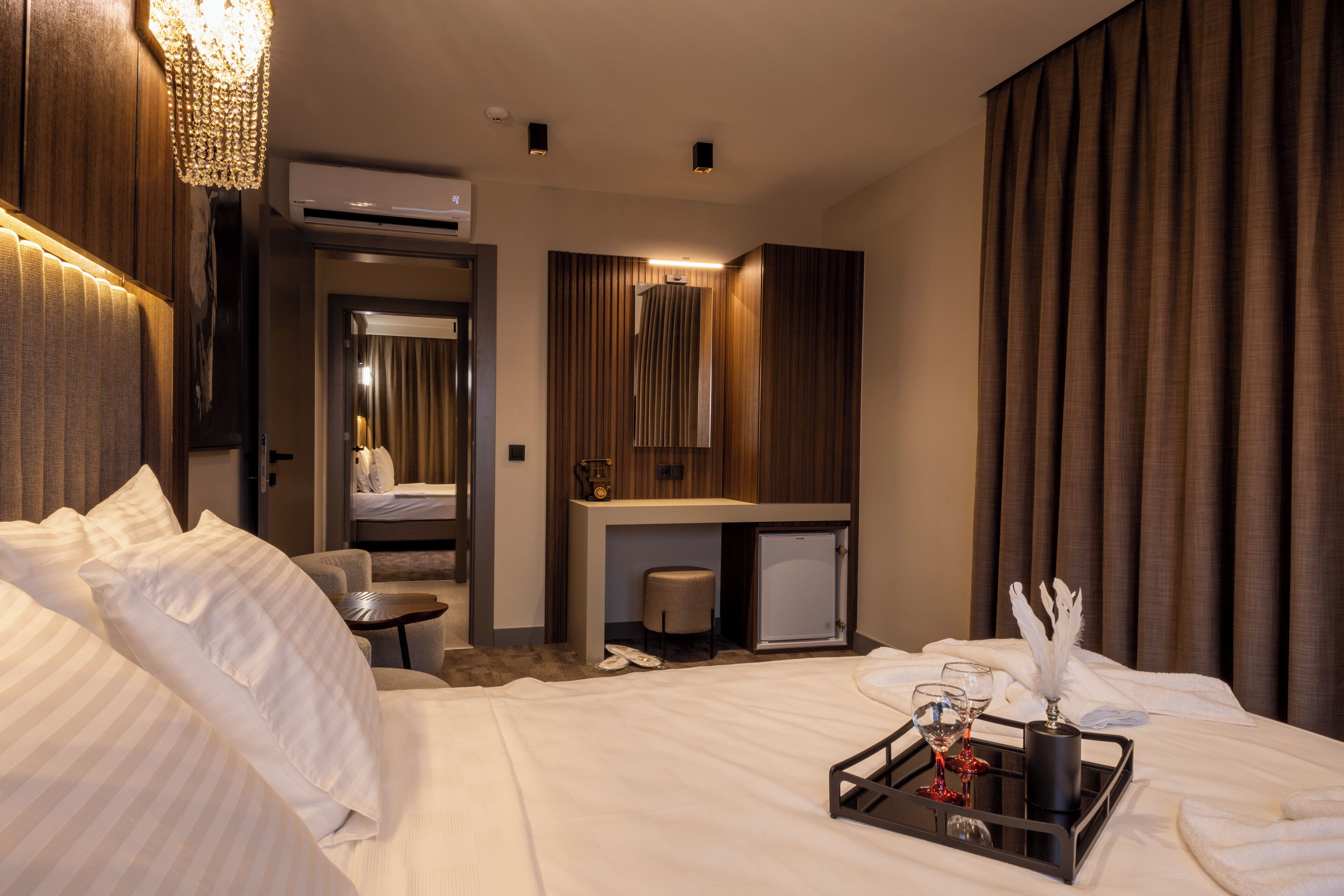 Una habitación de hotel con cama, escritorio, espejo y un refrigerador pequeño.
