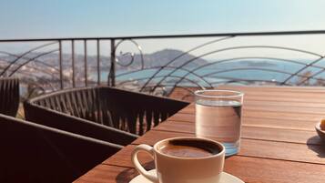 A wooden table with a cup of coffee and a glass of water, overlooking a scenic view of mountains and a body of water.