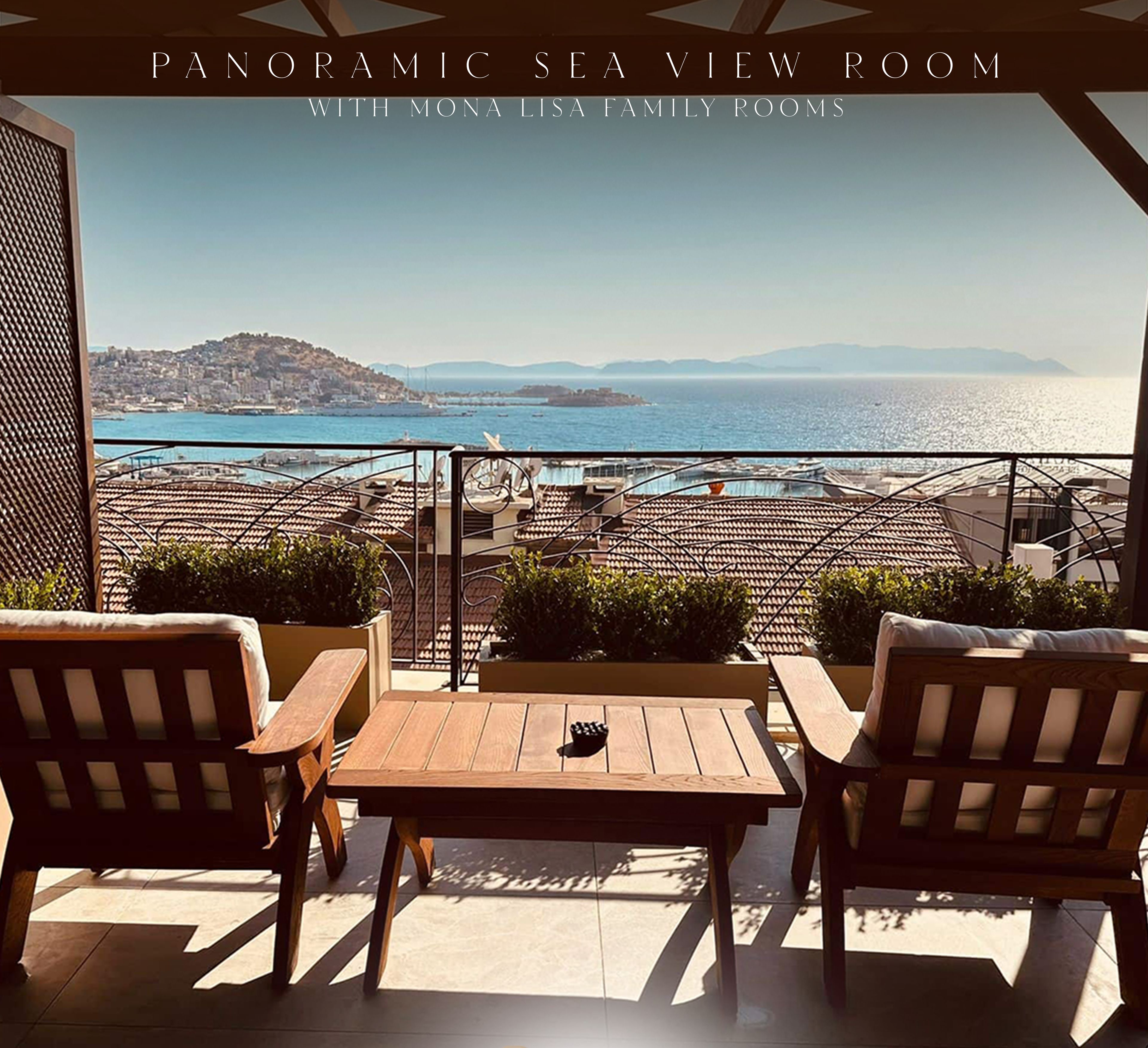 A panoramic sea view room with wooden furniture and a view of the sea and distant hills.