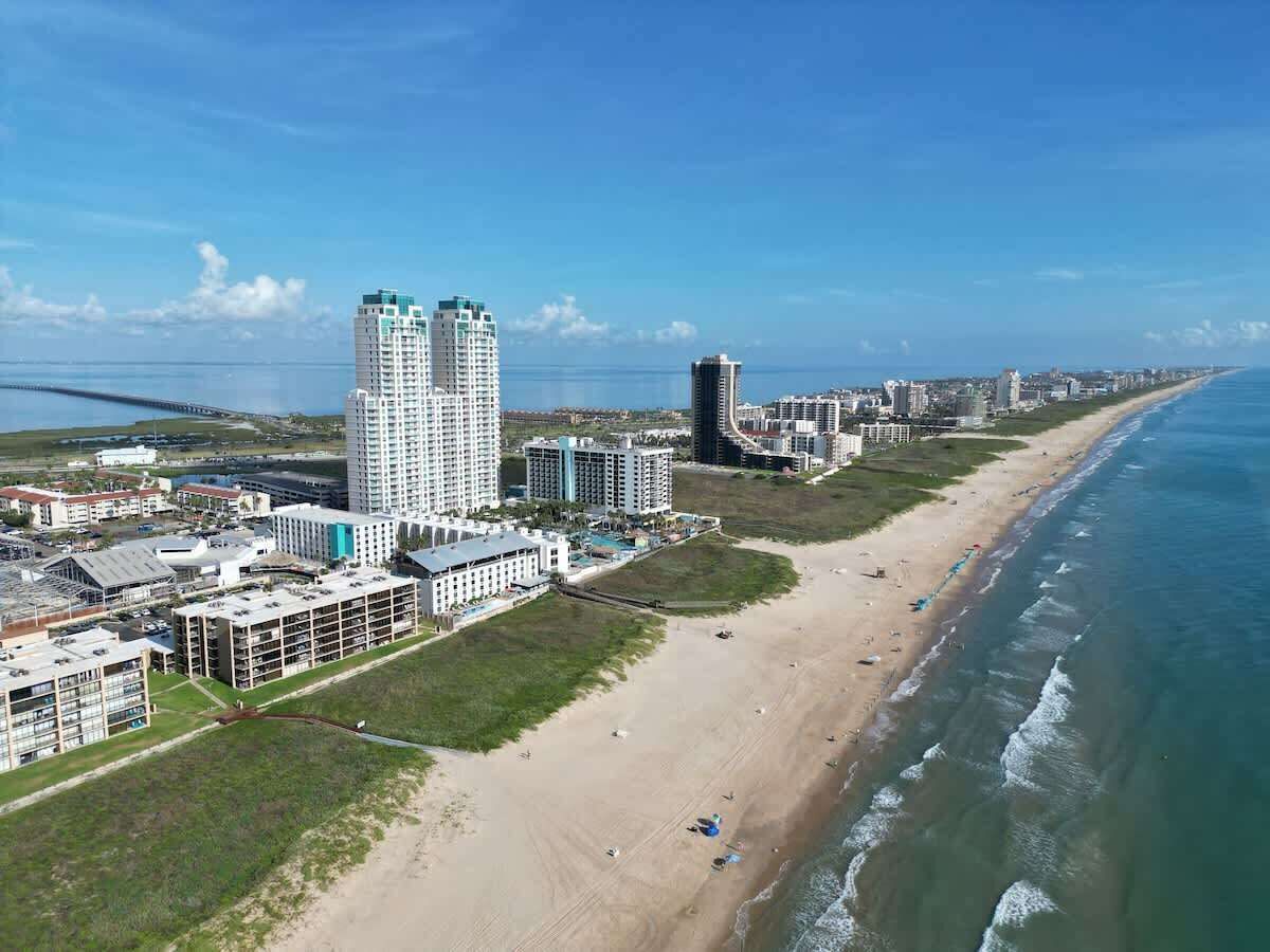 Eine Luftaufnahme einer Küstenregion mit Hochhäusern, einem Strand und einer Brücke.