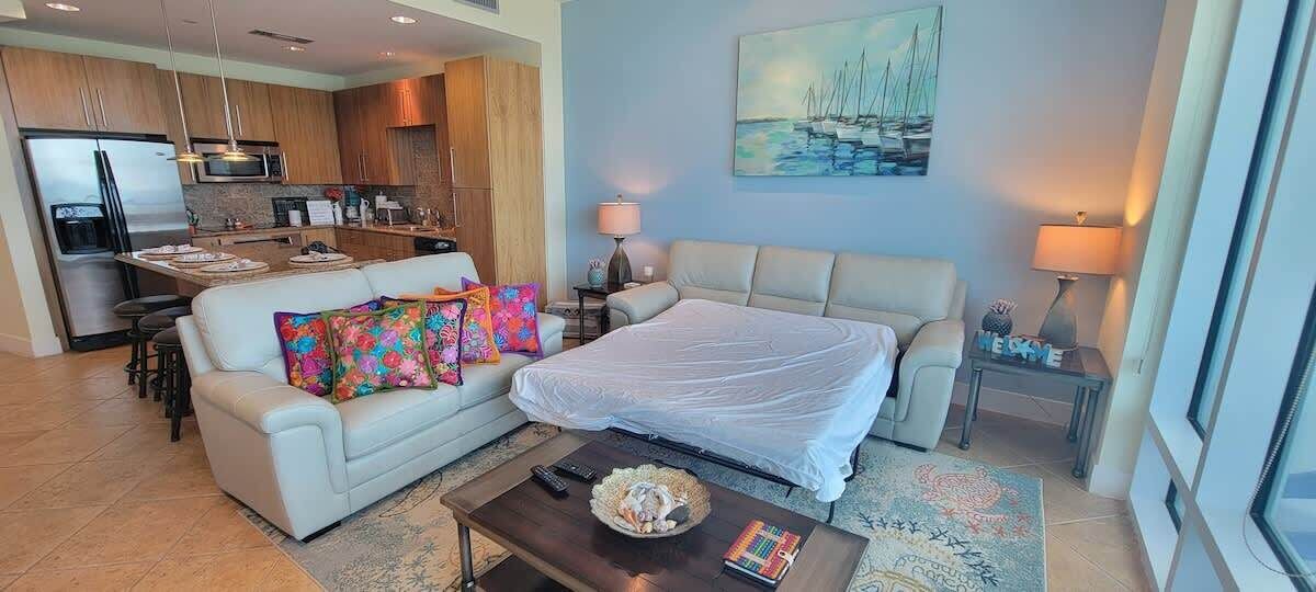 Una sala moderna con sofá, cama, mesa de centro y cocina al fondo.