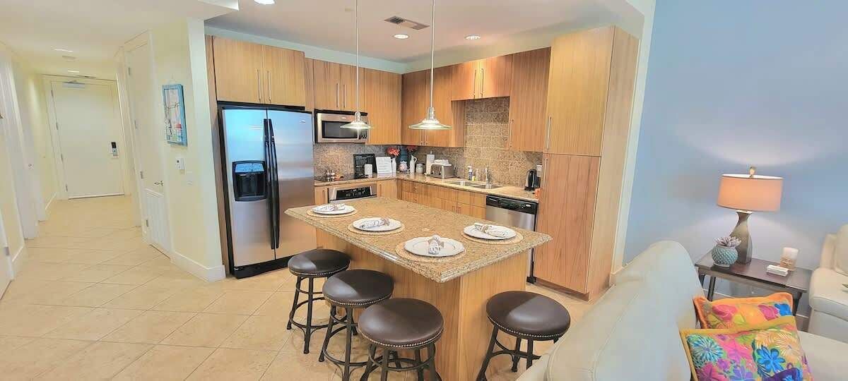 A modern kitchen with a central island, bar stools, and a dining area.