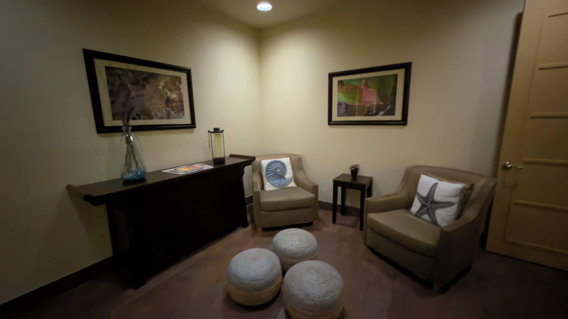 A corner room with a reception desk, two armchairs, a small table, and a door.