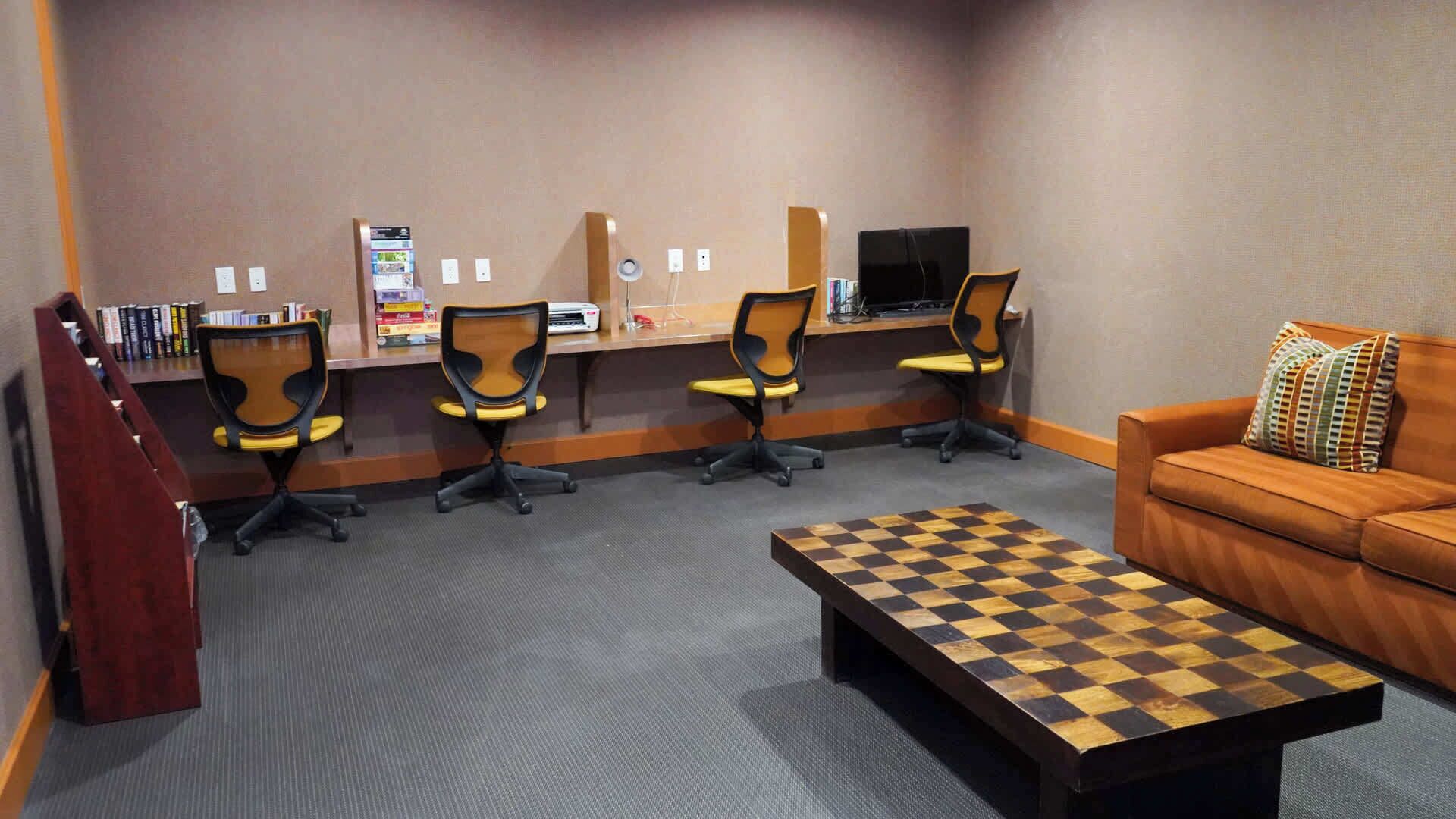 Una sala de conferencias con cuatro sillas, un escritorio, una computadora, un televisor y una mesa para jugar al ajedrez.