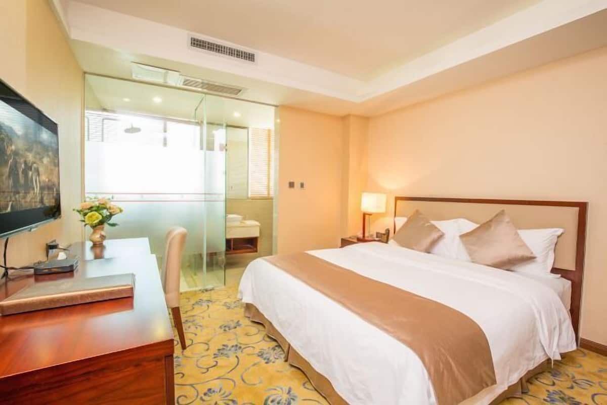 A hotel room with a bed, bedside table, TV, and a desk with a chair.