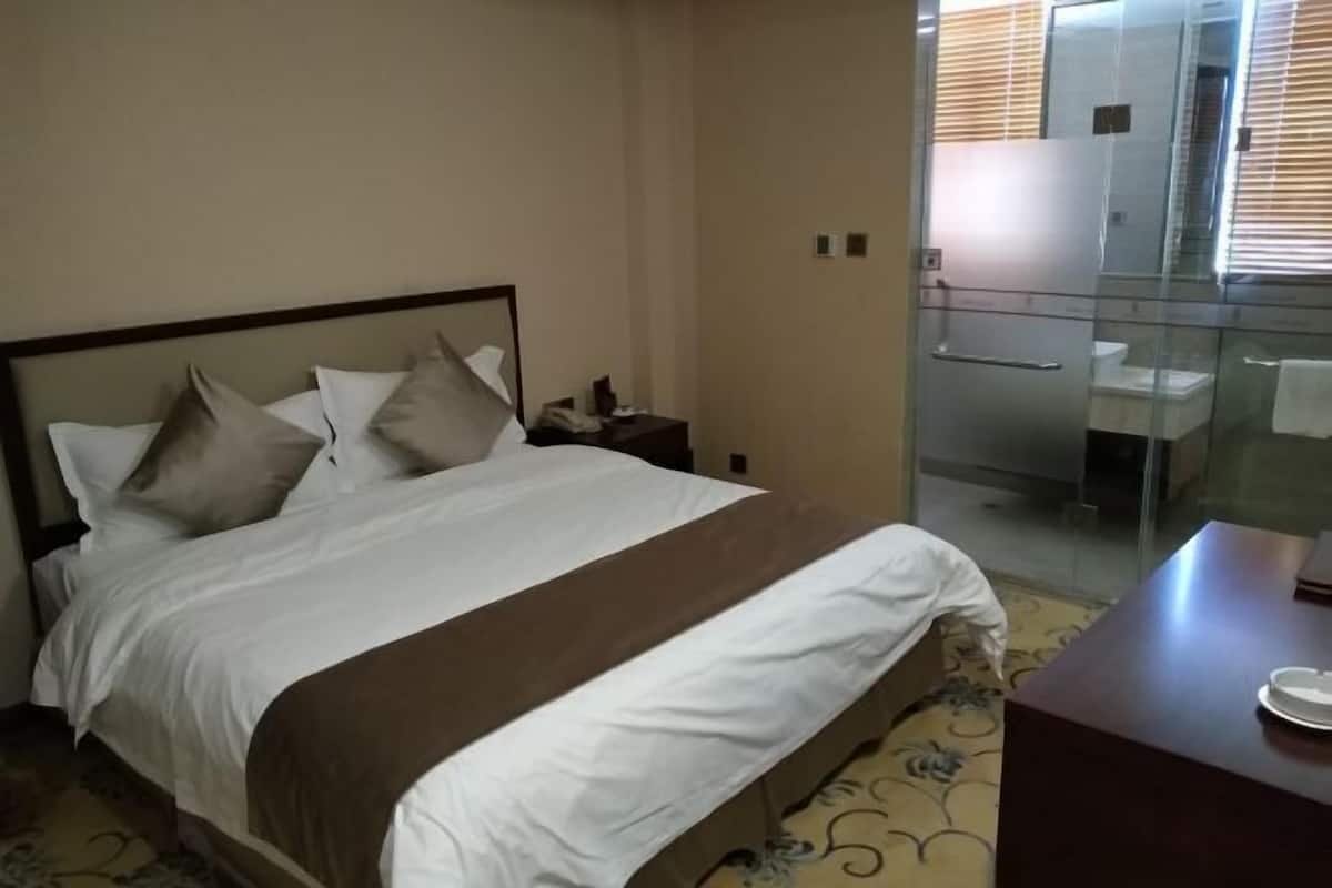 A hotel room with a bed, a bedside table, a glass-enclosed shower, and a small desk with a chair.